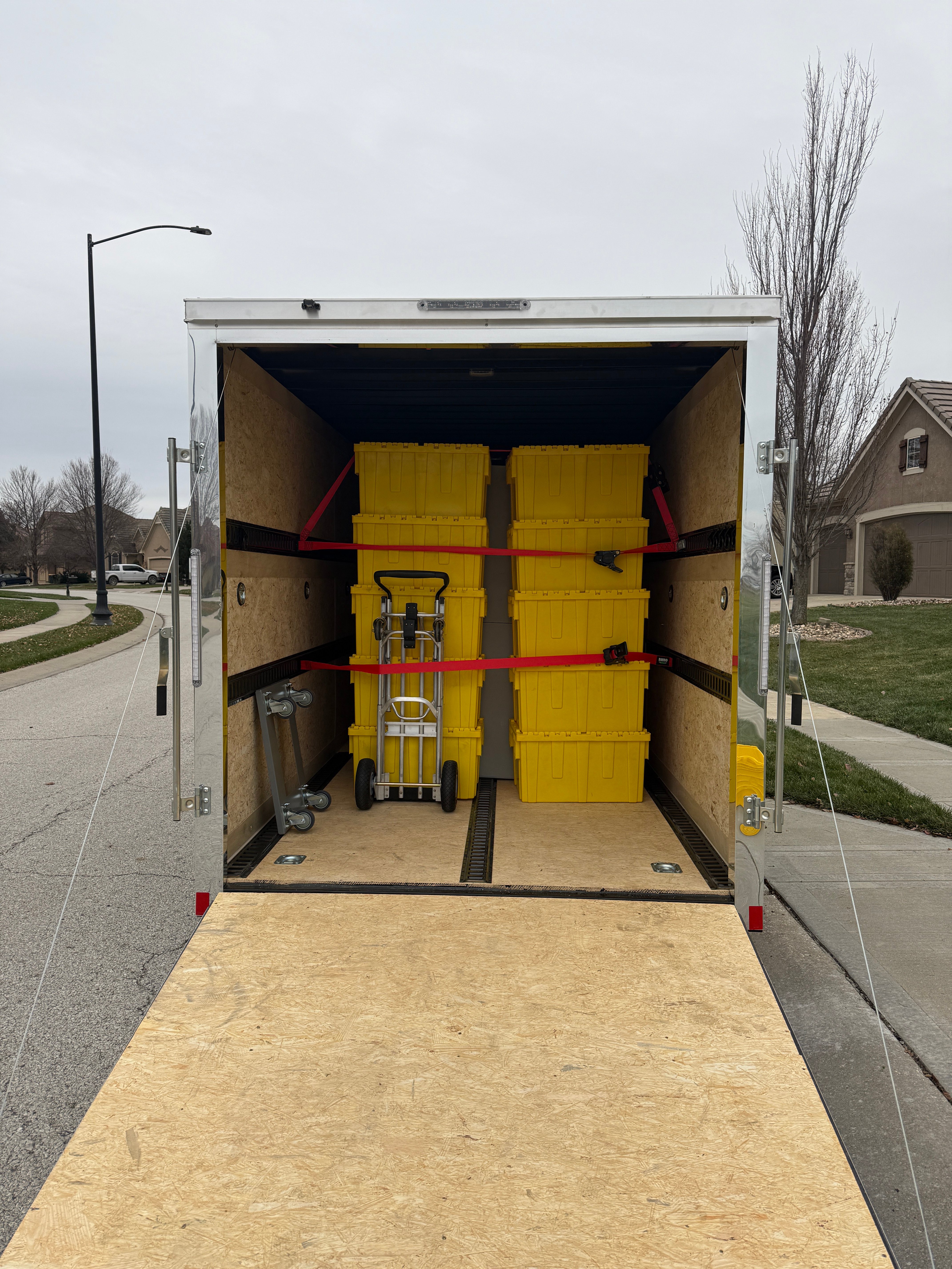 Trailer interior loaded with yellow moving storage bins secured with ratchet straps and hand truck
